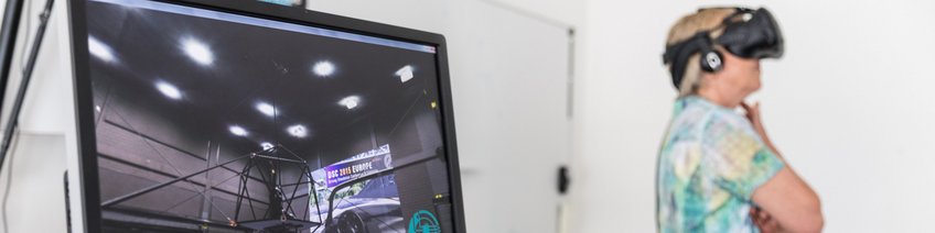 Equipment Bildschirm mit virtueller Simulation, Person mit VR-Headset im Hintergrund.