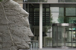 Ein Stockwerk hohe Steinskulpur der Minerva im Profil links neben dem Glasportal eines Bürogebäudes.