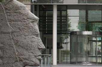 Der Science Hub von Amazon mit der Max-Planck-Gesellschaft, hier der Eingang der Generalverwaltung in München, ist die erste Einrichtung dieser Art außerhalb der USA. Ein Stockwerk hohe Steinskulpur der Minerva im Profil links neben dem Glasportal eines Bürogebäudes.
