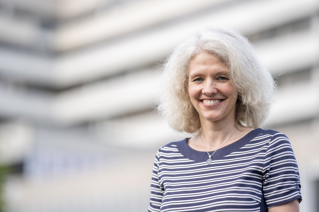 A portrait of Bettina Lotsch, Director at the Max Planck Institute for Solid State Research in Stuttgart, looking at the camera and smiling. She has shoulder-length white hair and is wearning a T-shirt with white and blue stripes.