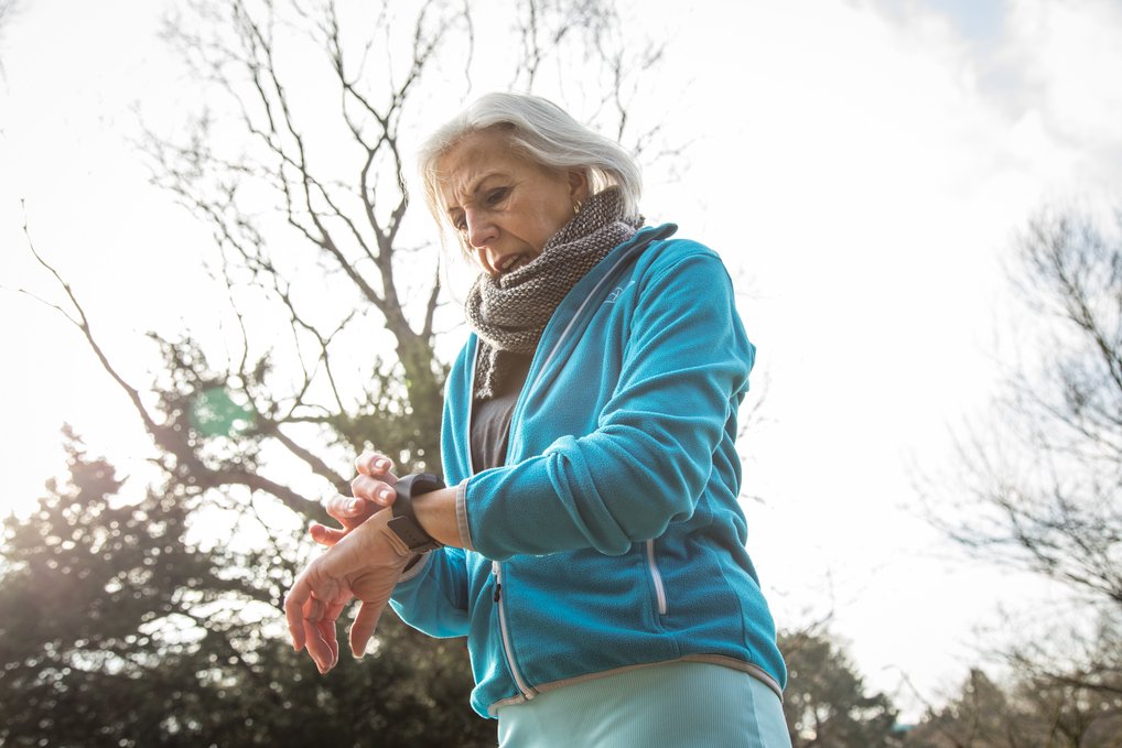 Person in blauer Jacke prüft Smartwatch im Freien.
