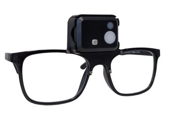 Brille mit Lichtsensor zum Messen der Lichtintensität am Auge. Schwarze Brille mit rechteckigem Rahmen und einer kompakten Kamera, die zentral auf dem oberen Steg des Rahmens montiert ist.