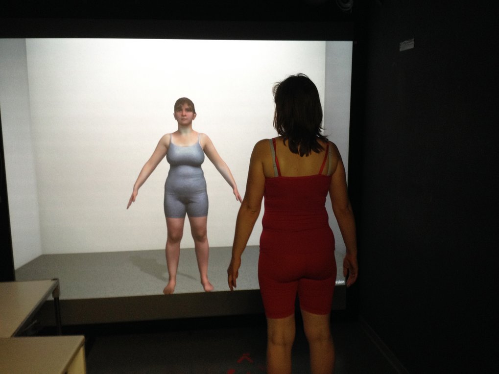 Individual in red clothing stands before a projected image in a dimly lit space.