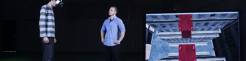Large Tracking Hall (TrackingLab) Person using VR headset, screen showing virtual environment with red blocks and cityscape.