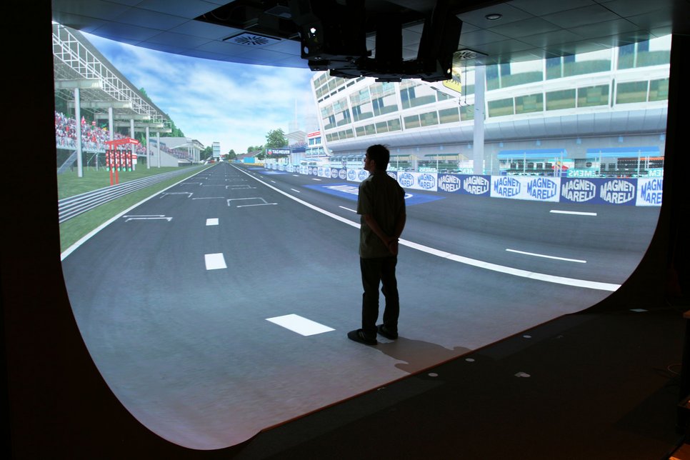 Eine Person steht in einem Rennstrecken-Simulator mit virtueller Projektion einer Rennstrecke.